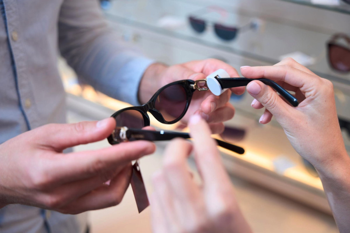 Kupac isprobava crne sunčane naočale u optici uz pomoć prodavača